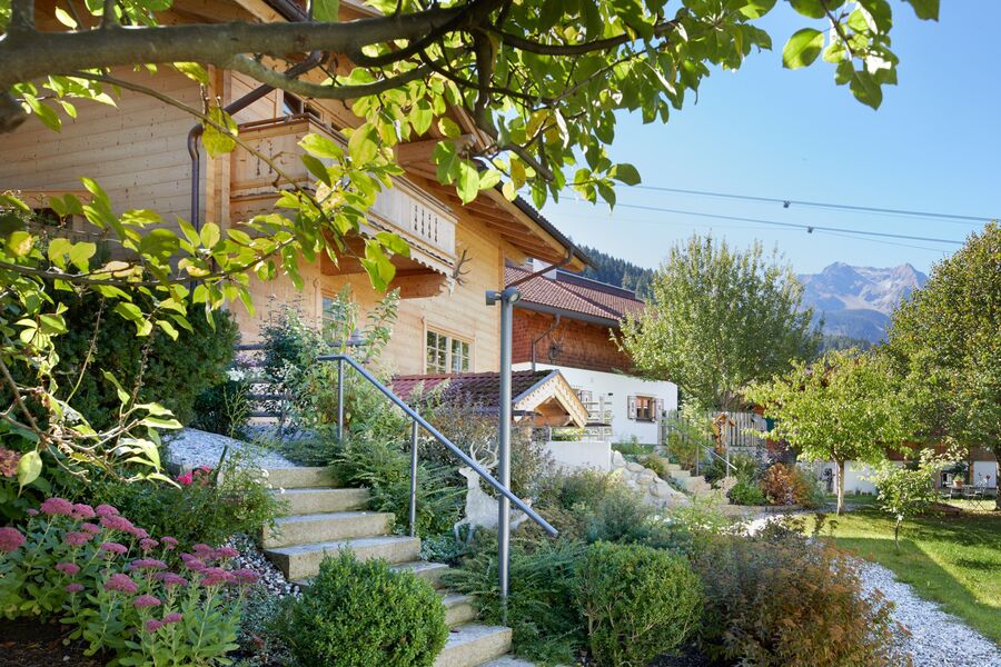 Stimmungsvolle Sommerlandschaft mit grünen Pflanzen und traditionell gestalteten Huber Chalets, umgeben von den Zillertaler Alpen.