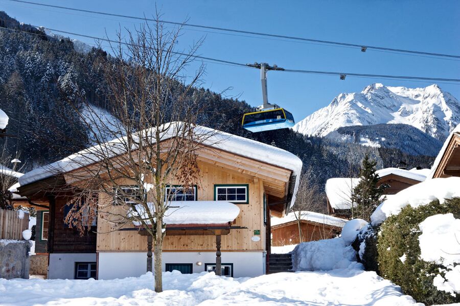 Huber Chalets in Mayrhofen mit Gondelbahn über den Dächern und einer malerischen Alpenkulisse im Hintergrund.