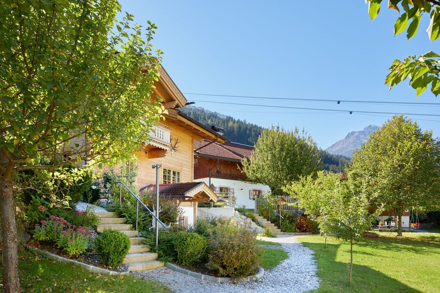 Helles Holzchalet in den Zillertaler Alpen, umgeben von grünen Wiesen und Bäumen bei strahlendem Sonnenschein.
