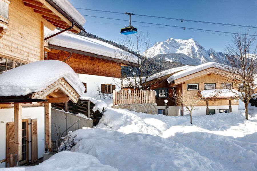 Huber Chalets in Mayrhofen im Zillertal im Winter mit schneebedeckten Dächern und einer vorbeifahrenden Seilbahn im Hintergrund.