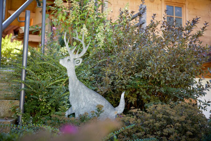 Eine stilvolle Metallskulptur eines Hirsches ziert den üppigen Garten der Huber Chalets in Mayrhofen, Zillertal.