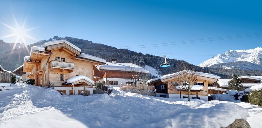 Die Huber Chalets in Mayrhofen im Zillertal, umgeben von tiefem Schnee, mit strahlendem Sonnenschein und den schneebedeckten Alpen im Hintergrund.