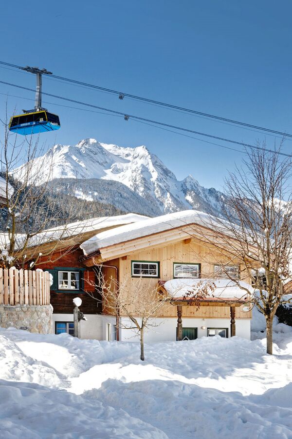 Die Huber Chalets in Mayrhofen, eingebettet in die verschneite Berglandschaft des Zillertals, mit Blick auf die Seilbahn und die Alpen.